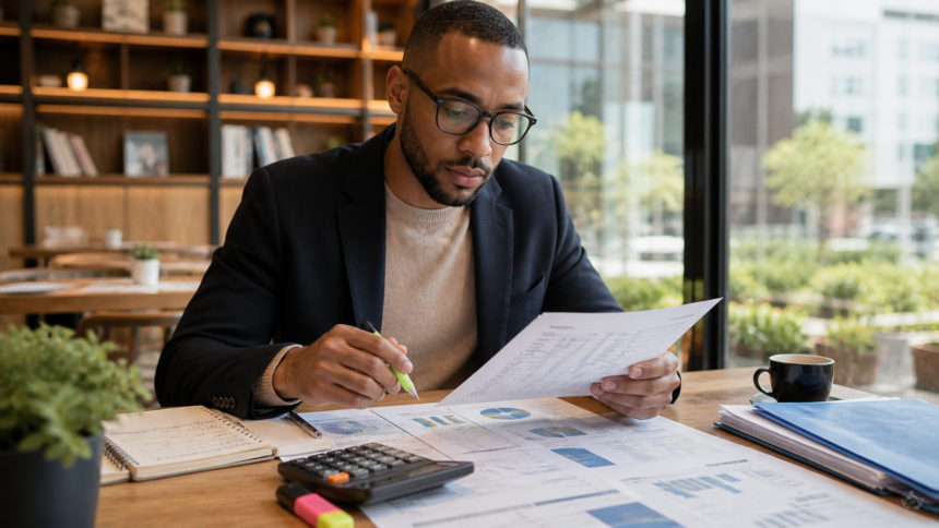 Analyste financier en costume analysant des rapports boursiers avec surligneur et graphiques sur son bureau